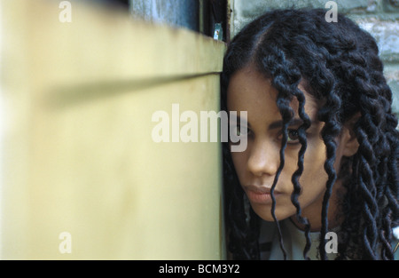 Young woman huddled in the corner, looking at camera Stock Photo