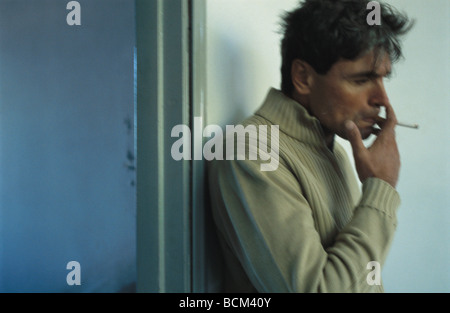 Mature man smoking cigarette, leaning against wall next to open doorway Stock Photo