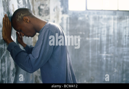 Young man leaning with head and hands against wall Stock Photo