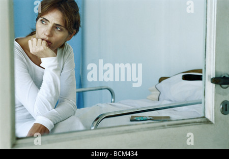 Woman sitting on hospital bed, hand under chin, looking away Stock Photo