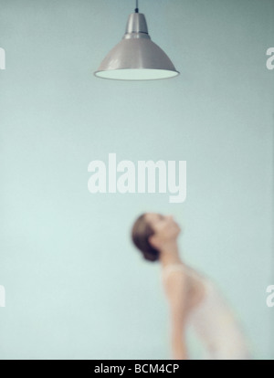 Young woman bending over backwards under ceiling lamp, focus on lamp in foreground Stock Photo