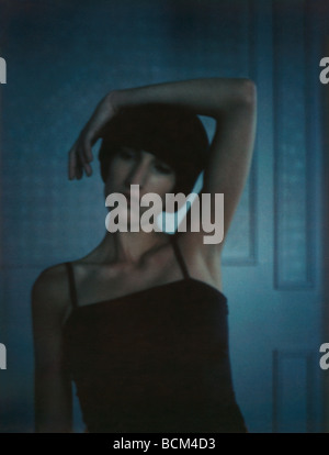 Young woman standing with arm around head, looking away, portrait Stock Photo
