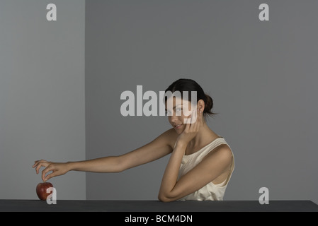 Woman holding apple by its stem, looking sideways at camera Stock Photo