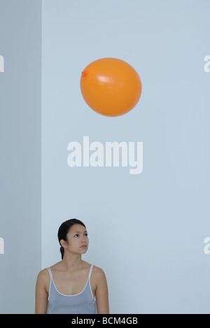 Orange balloon floating over woman's head, woman looking away Stock Photo