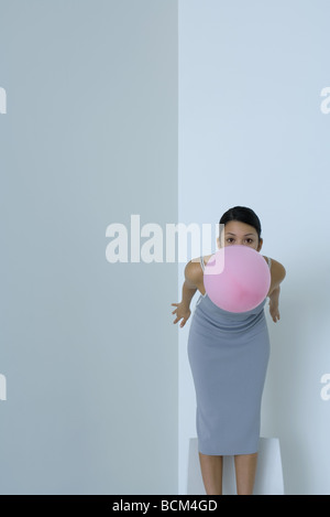 Woman bending over, holding balloon in mouth, looking at camera Stock Photo