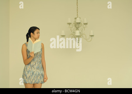 Woman holding book, frowning in direction of unlit chandelier Stock Photo