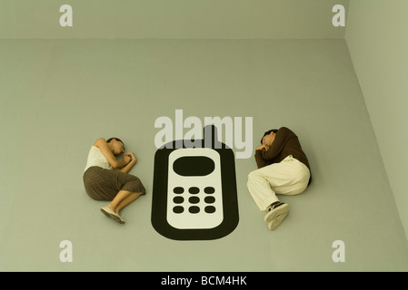 Man and woman lying down on the ground with large cell phone graphic between them Stock Photo