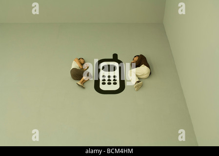 Man and woman lying down on the ground with large cell phone graphic between them Stock Photo