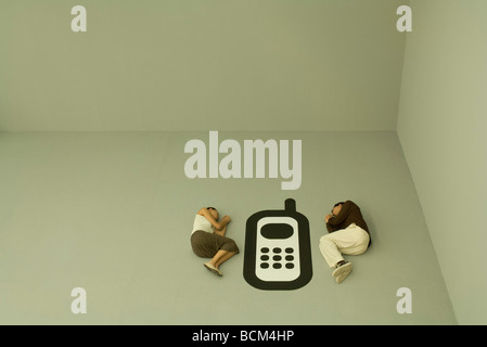 Man and woman lying down on the ground with large cell phone graphic between them Stock Photo