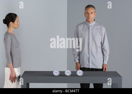 Man and woman standing by table with line of clocks, man looking at camera Stock Photo