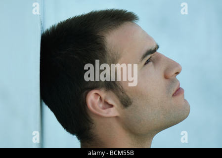 Man leaning head against wall, looking up, profile Stock Photo