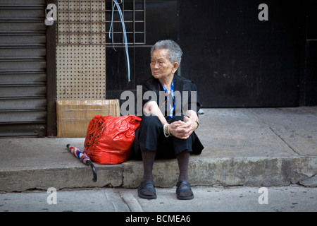 Woman waiting eagerly on the step in front of a still colsed store in Chinatown, Manhattan, NY, USA 2008 Stock Photo