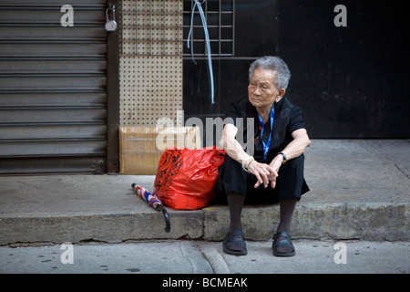 Woman waiting eagerly on the step in front of a still colsed store in Chinatown, Manhattan, NY, USA 2008 Stock Photo