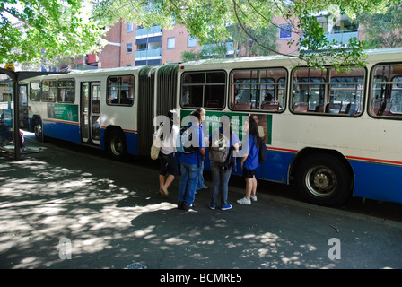 Schoolchildren chat next to an old bendy bus. Stock Photo