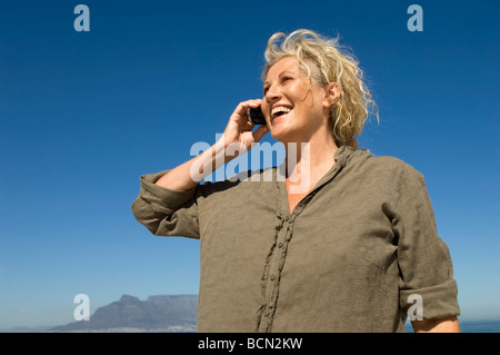 Senior woman talking on mobile phone while standing on beach, Table View Stock Photo