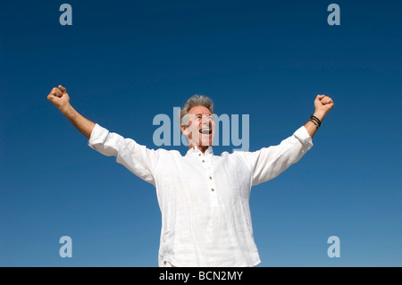 Low angle view of senior man cheering with arms outstretched, Table View Stock Photo