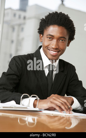 Businessman smiling leaning on a football at his desk Stock Photo