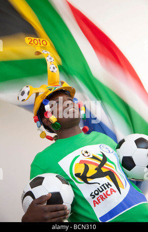 Young man wearing a traditional soccer Makaraba and holding soccer balls with the South African flag flying Stock Photo