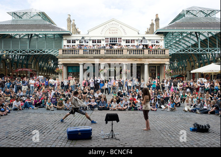 A street entertainer performs to a large crowd of tourists in Covent Garden, London. Stock Photo