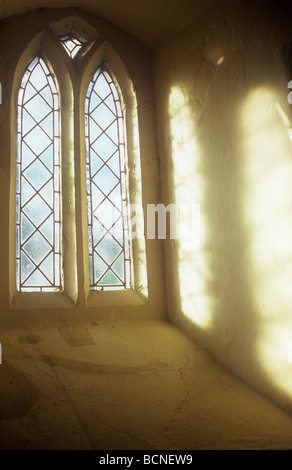 Soft light streaming through two upright frosted diamond leaded windows and projected onto cream wall of deep recess Stock Photo