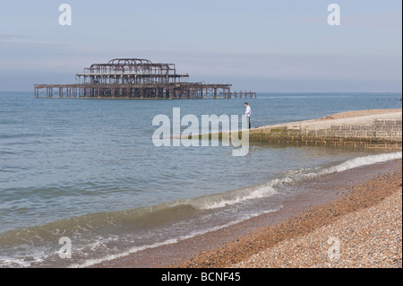 Solitary man looks out over the sea and remains of fire damaged pier alone on a jetty alongside a  shingle beach at Brighton. Stock Photo