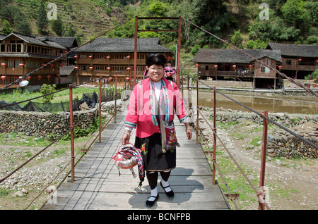 Yao woman crossing river on suspension bridge Huangluo Village Guangxi China Stock Photo