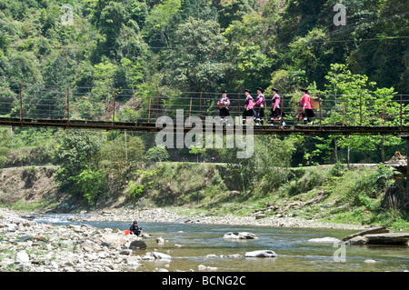 Group of Yao women crossing river on suspension bridge Huangluo Village Guangxi China Stock Photo