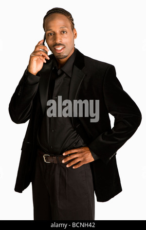African American man wearing black suit, standing and holding cell phone. He is talking on his cell phone with hand on one hip. Stock Photo