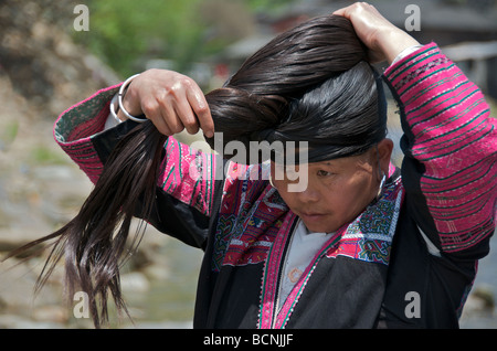 Yao Long Hair woman tying extremely long black hair beside river Huangluo Village Guangxi China Stock Photo