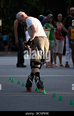 Mature Senior Man Rollerblading backwards whilst maneuvering his feet in between a line of green cones placed on the ground. Stock Photo