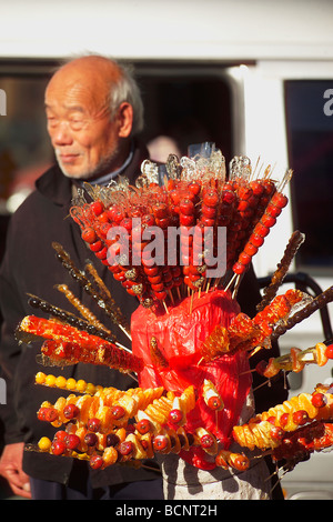 Elderly Chinese man selling traditional snack sugarcoated haws on a stick, Beijing, China Stock Photo