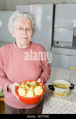 Frau in ihren Siebzigern steht in der Küche mit einer Schüssel geschälter Kartoffeln Stock Photo