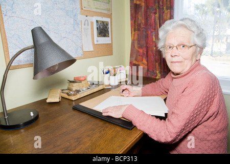 Frau in ihren Siebzigern sitzt am Schreibtisch und schreibt einen Brief