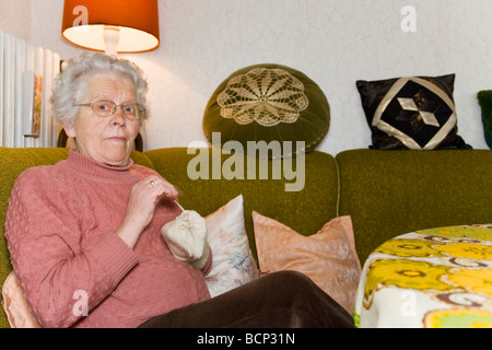 Frau in ihren Siebzigern sitzt im Wohnzimmer und stopft Wollsocken