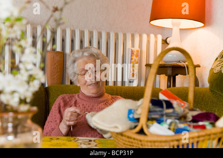 Frau in ihren Siebzigern sitzt im Wohnzimmer und stopft Wollsocken