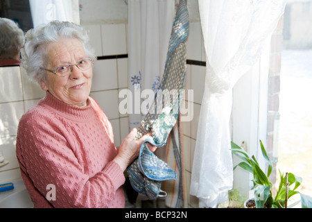 Frau in ihren Siebzigern steht in der Küche und trocknet sich die Hände ab Stock Photo