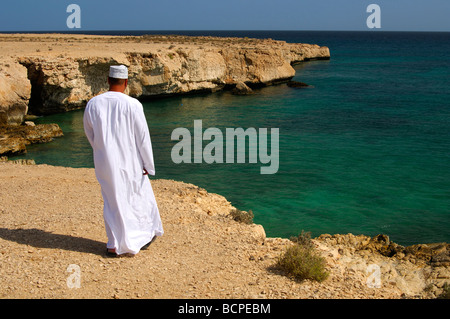 Omani man wearing traditional dishdashi robe or thawb clothing standing on a rocky cliff, Sultanate of Oman Stock Photo