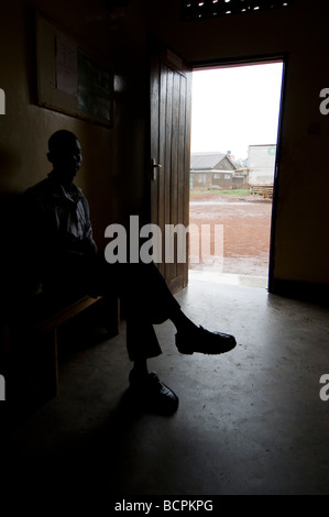 African man sitting in dark room lit by open door waiting Stock Photo