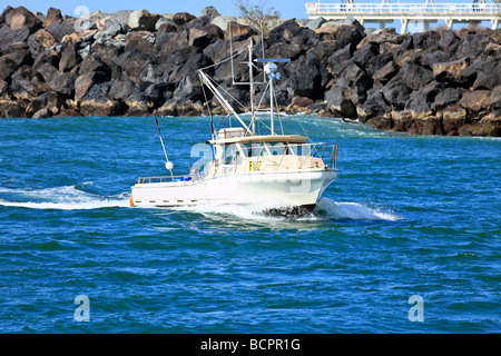 Small fishing boat moving through a breakwater to its mooring Stock Photo