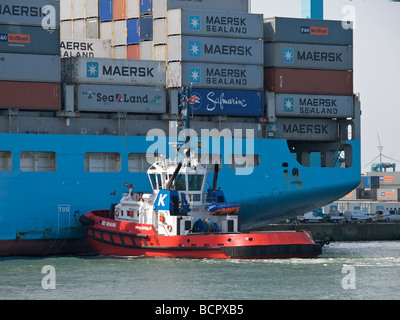 Tug boat nudging a very large container ship in the port of Rotterdam Zuid Holland the Netherlands. Tug markings visible Stock Photo