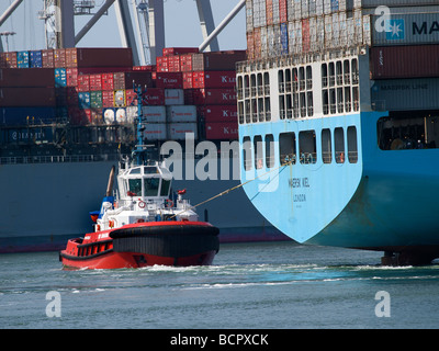 Tug boat pulling a very large container ship in the port of Rotterdam Zuid Holland the Netherlands Stock Photo