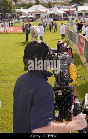 Professional digital video cameraman recording film footage at an outdoor cattle ring in an agricultural show. Stock Photo