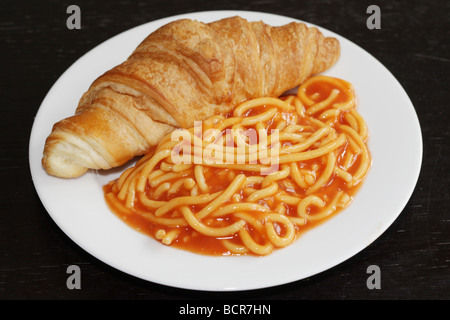 Alternate Breakfast Idea Of A Freshly Baked Croissant with Tinned Spaghetti In Tomato Sauce Against A Black Background With No People Stock Photo