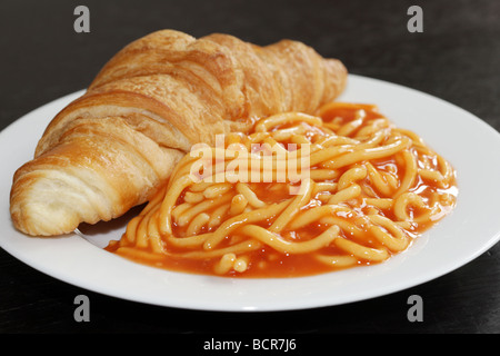 Alternate Breakfast Idea Of A Freshly Baked Croissant with Tinned Spaghetti In Tomato Sauce Against A Black Background With No People Stock Photo