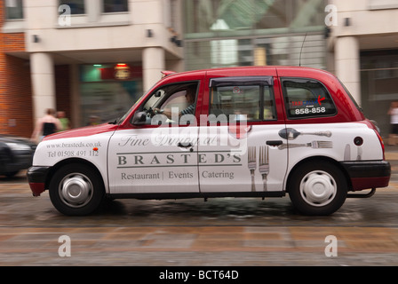 A taxi driving through the city centre in the rain showing movement in Norwich Norfolk Uk Stock Photo