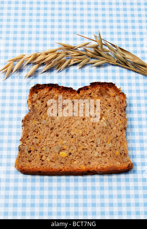 Single slice of bread, wholemeal bread with pumpkin and sunflower seeds on blue and white tablecloth, with oats Stock Photo