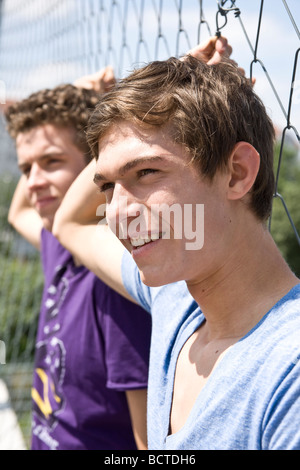 Two guys leaning against a fence, cool, looking into the distance Stock Photo