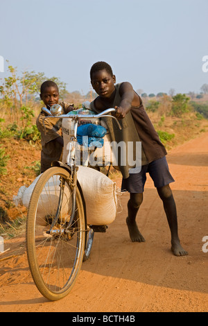 Two local boys carrying heavy bags on a bicycle, Zambia, Africa Stock Photo