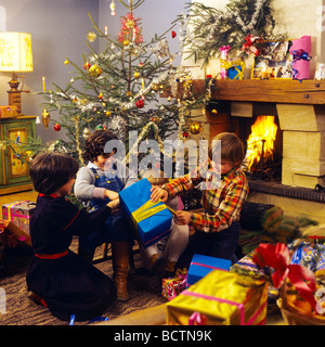 3 CHILDREN OPENING CHRISTMAS PRESENTS UNDER THE TREE family christmas presents tree opening Stock Photo
