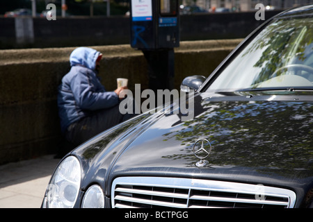 street beggar lying beside a parking ticket machine and mercedes car looking for spare change dublin city showing inequality Stock Photo